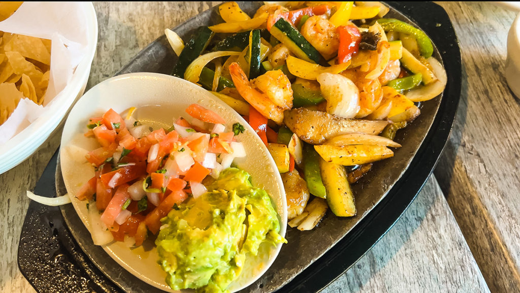a colorfuil plate of fajita vegetables and a bowl of guacamole and salsa on a table.